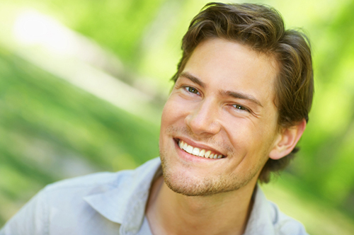 Young man smiling with green natural background iStock 000003447076Small width of 500 pixels